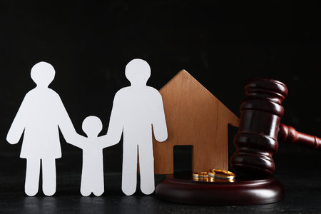 Judge's gavel with wooden house, figures of family and rings on black backgroundの写真素材