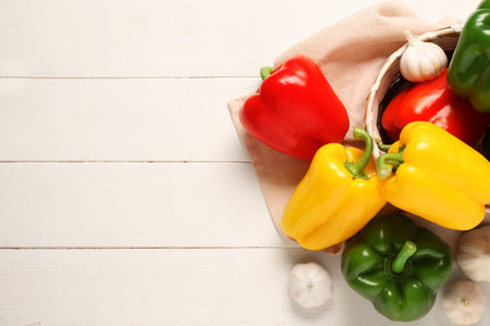 Wicker bowl with fresh colorful bell peppers and garlic on white wooden backgroundの写真素材