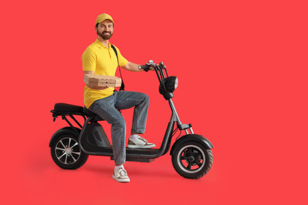 Male courier with pizza boxes riding electric bike on red backgroundの写真素材
