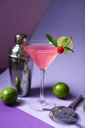 Glass of tasty Cosmopolitan cocktail garnished with cherry and lime on purple backgroundの写真素材