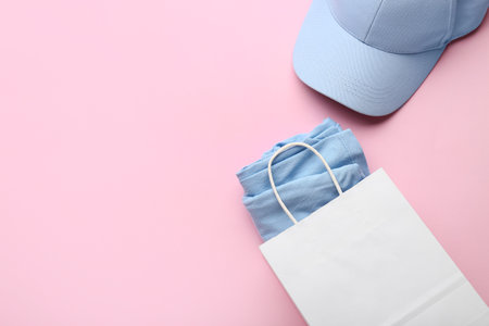 Paper shopping bag with stylish t-shirt and cap on pink backgroundの写真素材