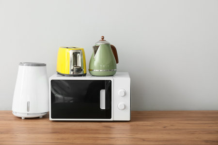 Microwave oven with electric kettle, air purifier and toaster on wooden table against white wallの写真素材