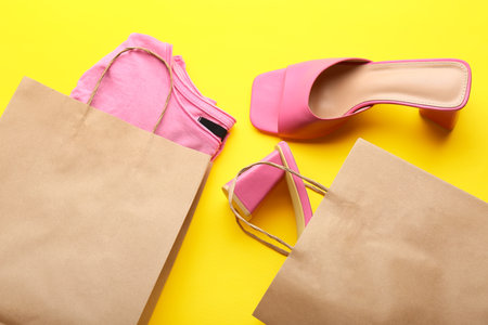 Paper shopping bags with stylish t-shirt and high heels on yellow backgroundの写真素材