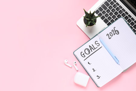 Notebook with 2026 goals, earphones and laptop on pink backgroundの写真素材