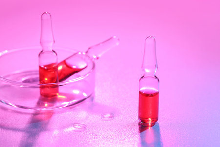 Glass ampoules with Petri dish on color background
