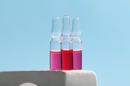 Glass ampoules on podium against light blue backgroundの写真素材