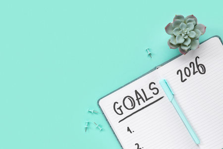 Notebook with 2026 goals, plant and paper pins on green background