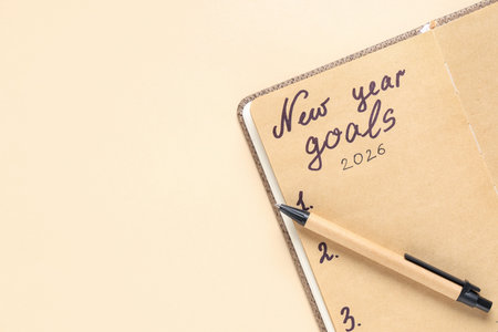 Notebook with text NEW YEAR GOALS 2026 on beige background, closeup