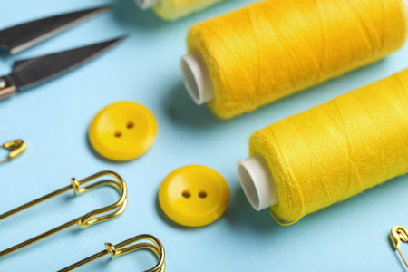Composition with thread spools, pins and buttons on blue background, closeup