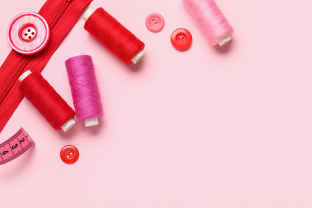 Composition with thread spools, zipper and buttons on pink background, closeupの写真素材
