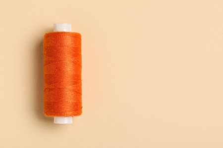 Orange sewing thread spool on beige background, closeupの写真素材
