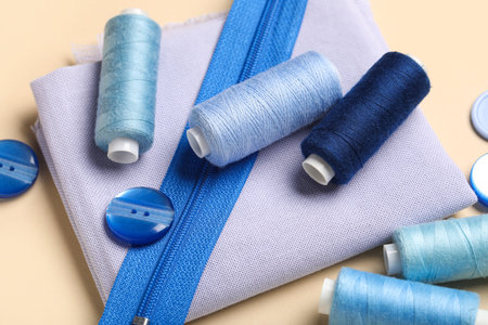 Composition with thread spools, fabric and zipper on beige background, closeup