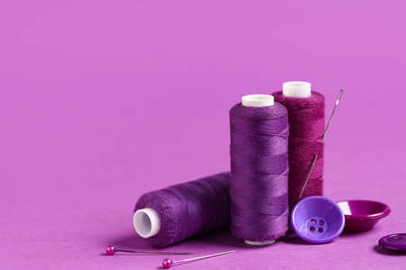 Spool of thread with needle, ball pins and buttons on purple backgroundの写真素材