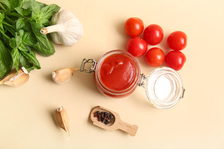 Jar of tasty tomato sauce with garlic, peppercorns and basil leaves on beige backgroundの写真素材
