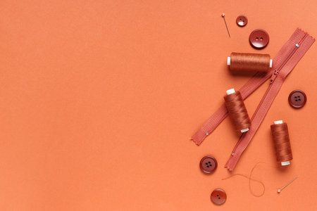Spools of thread with buttons, zipper and ball pins on brown backgroundの写真素材