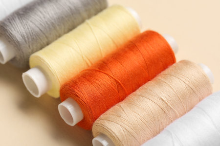 Set of different thread spools on beige background, closeup