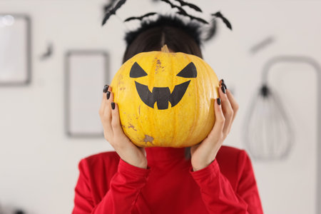 Beautiful young happy woman dressed for Halloween with pumpkin in living roomの写真素材