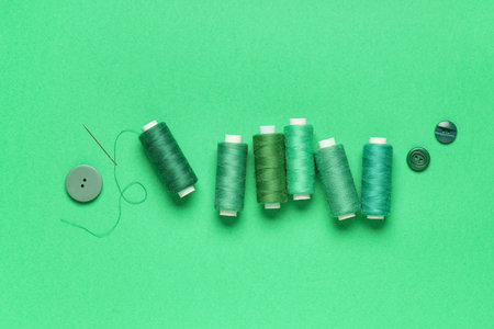 Spools of thread with needle and buttons on green background