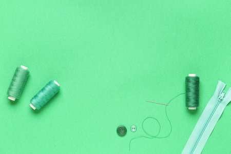 Spools of thread with needle, buttons and zipper on green backgroundの写真素材