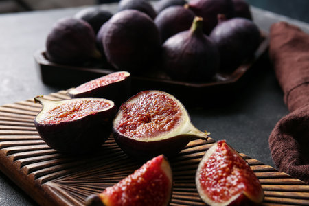 Wooden board with cut fresh ripe figs on black background, closeup