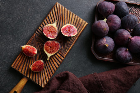 Wooden board and tray with fresh ripe figs on black background
