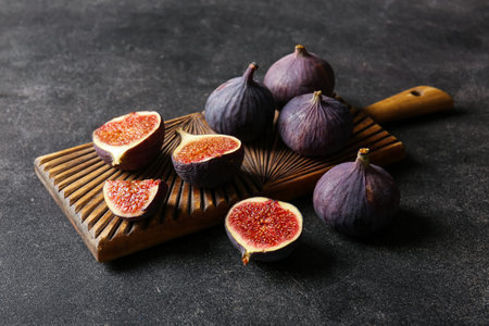 Wooden board with fresh ripe figs on black background