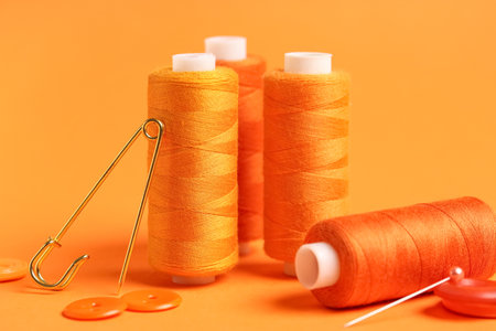 Spools of thread with buttons and ball pin on orange backgroundの写真素材