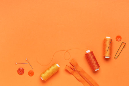 Spools of thread with ball pins, buttons and zipper on orange backgroundの写真素材