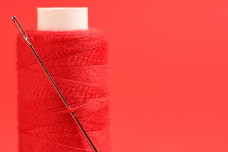 Spool of thread with needle on red background, closeupの写真素材