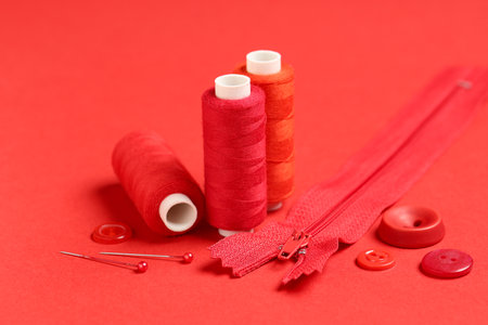 Spools of thread with ball pins, zipper and buttons on red backgroundの写真素材