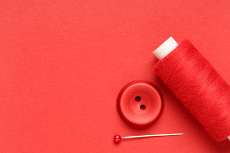 Spool of thread with ball pin and button on red backgroundの写真素材