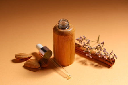 Composition with bottle of essential oil, dried flowers and cinnamon stick on orange background, closeupの写真素材
