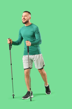 Sporty young man with walking poles on green backgroundの写真素材