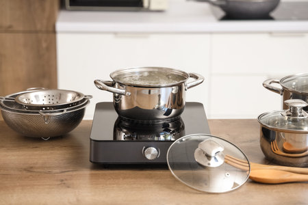 Cooking pot with boiling water on mini stove in kitchen