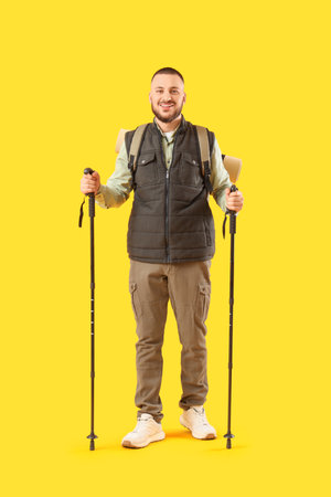 Young man with walking poles on yellow backgroundの写真素材