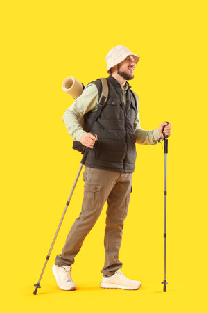 Young man in hat with walking poles on yellow backgroundの写真素材