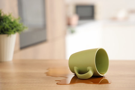 Overturned green cup and spilled coffee on table in kitchen, closeupの写真素材