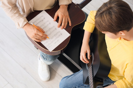 Private music teacher with note sheet giving guitar lessons to boy in room, top viewの写真素材