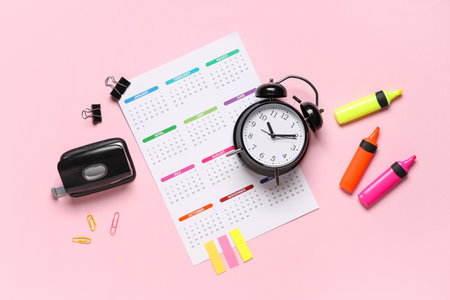 Calendar with alarm clock, markers, hole puncher and stickers on pink backgroundの写真素材