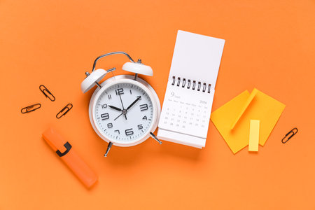 Calendar with alarm clock, sticky notes, marker, stickers and paper clips on orange backgroundの写真素材