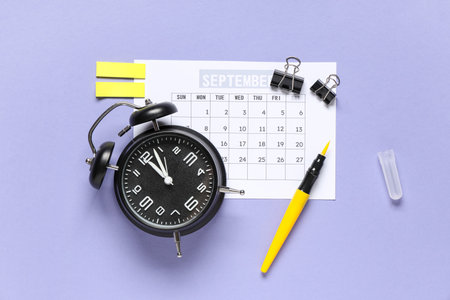 Calendar with alarm clock, felt tip pen, stickers and binder clips on purple backgroundの写真素材