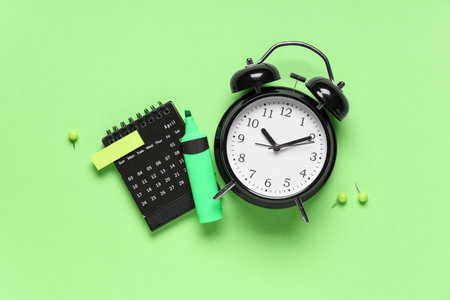 Calendar with alarm clock, paper pins, stickers and marker on green backgroundの写真素材