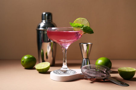 Glass of tasty Cosmopolitan cocktail with lime and bartender tools on brown backgroundの写真素材