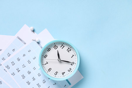 Calendar with alarm clock and paper pins on blue backgroundの写真素材