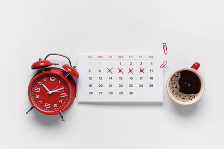 Calendar with alarm clock, paper clips and cup of coffee on white backgroundの写真素材