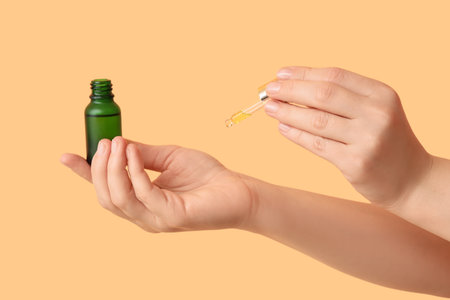 Female hands with bottle of essential oil on beige backgroundの写真素材