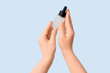 Female hands with bottle of essential oil on light backgroundの写真素材