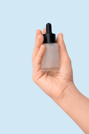 Female hand with bottle of essential oil on light backgroundの写真素材