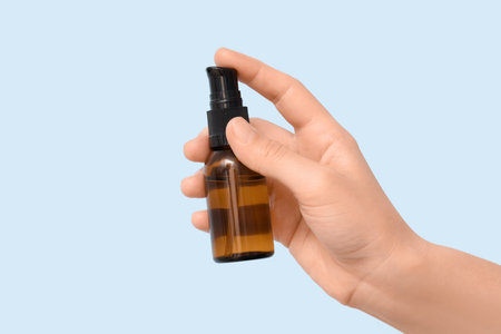 Female hand with bottle of essential oil on light background