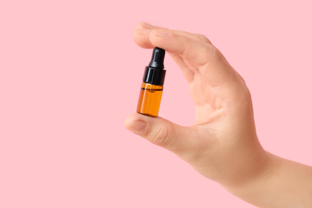 Female hand with bottle of essential oil on pink backgroundの写真素材